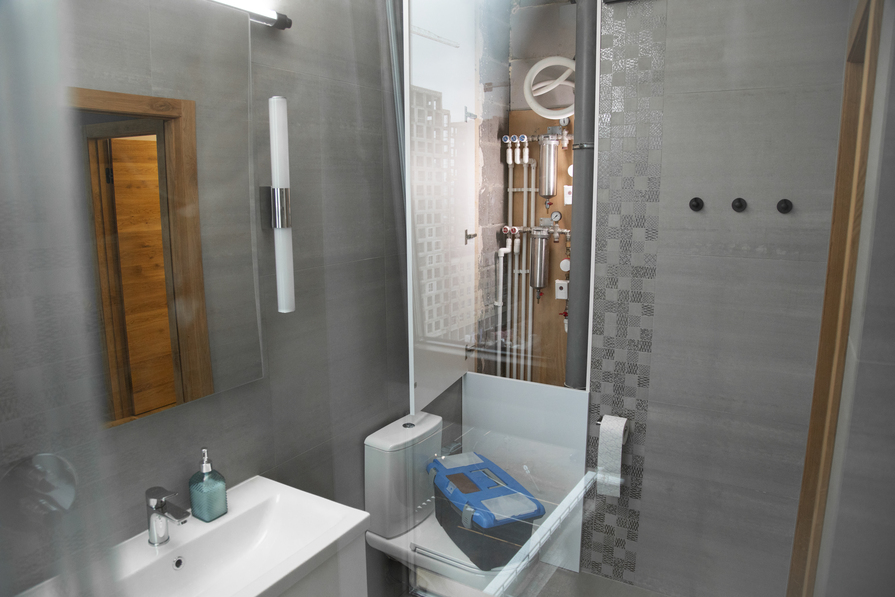 Badezimmer mit sichtbaren Rohren und einem bereitstehenden Werkzeugkasten für Reparaturen.