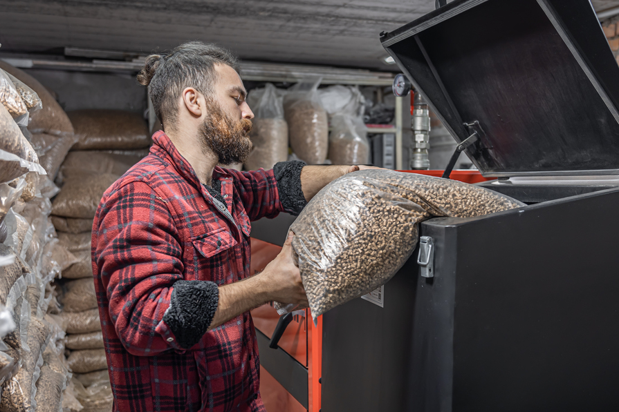 Mann füllt Holzpellets in einen Pelletkessel zur umweltfreundlichen und effizienten Beheizung eines Hauses.