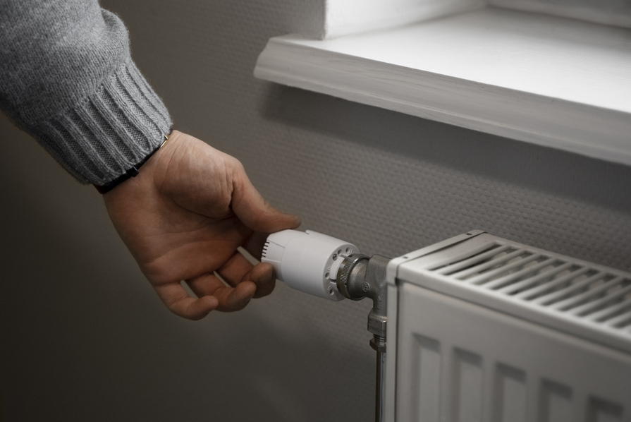 Hand dreht am Thermostat eines Heizkörpers zur Regulierung der Raumtemperatur und zum Energiesparen.