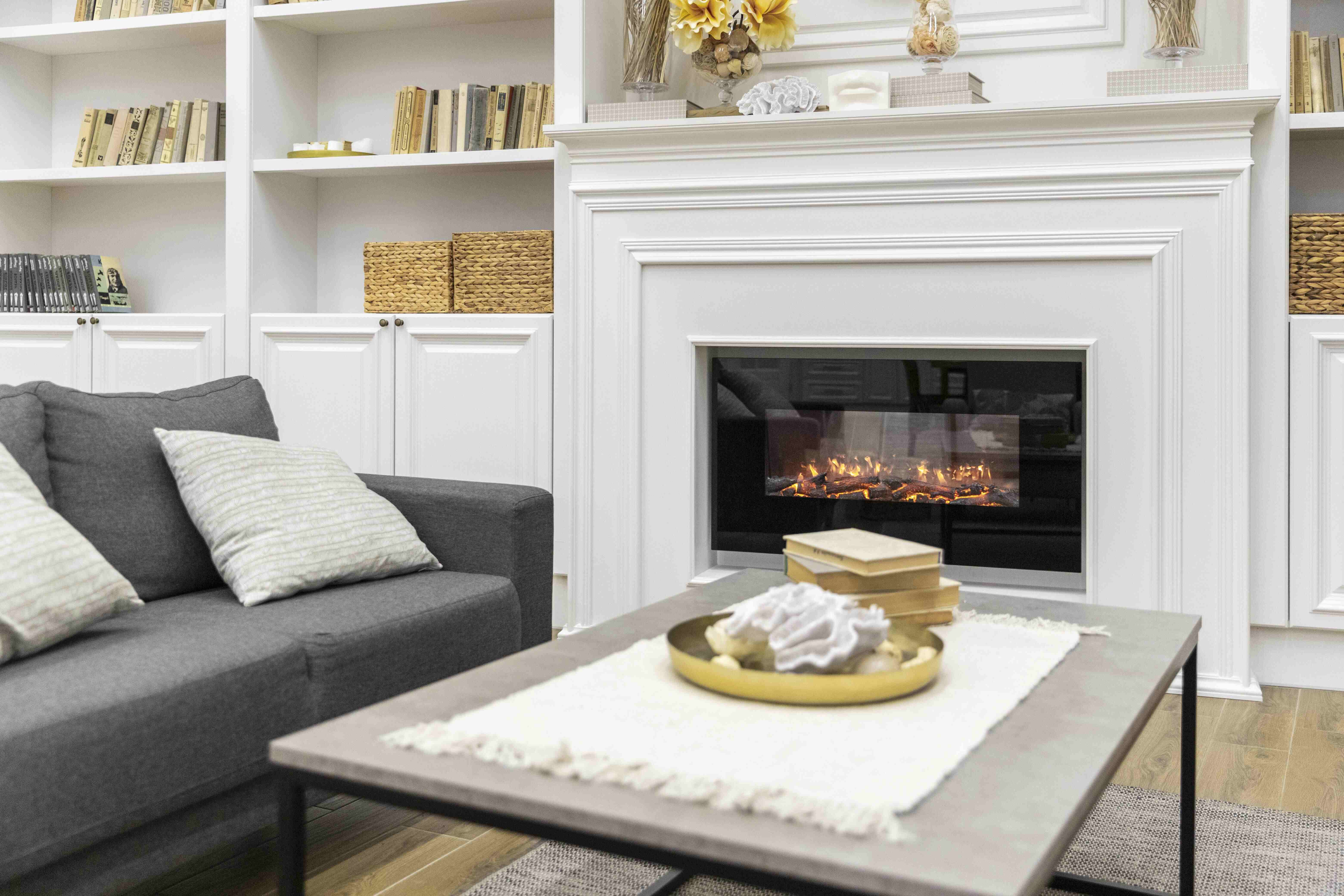 Modernes Wohnzimmer mit grauem Sofa, Kamin mit Flammenoptik, Bücherregalen und dekoriertem Couchtisch.
