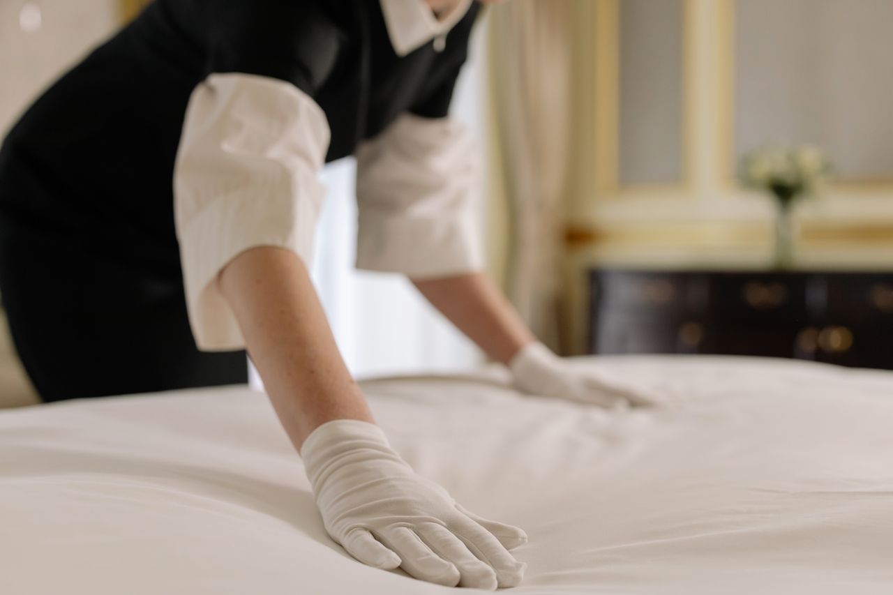 Hotelmitarbeiterin glättet mit weißen Handschuhen eine frisch bezogene Matratze.