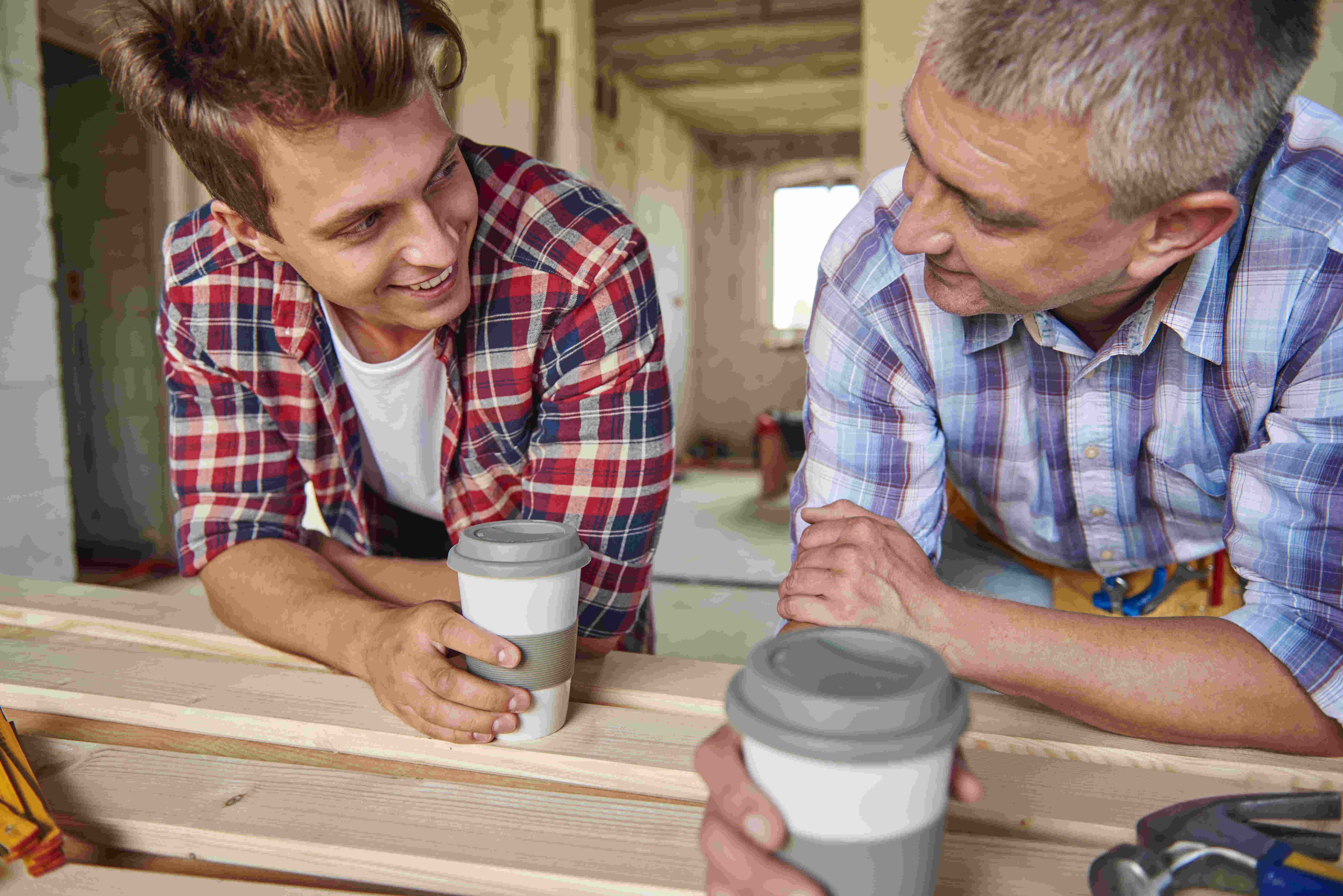 Zwei Handwerker machen eine Kaffeepause und unterhalten sich auf der Baustelle.