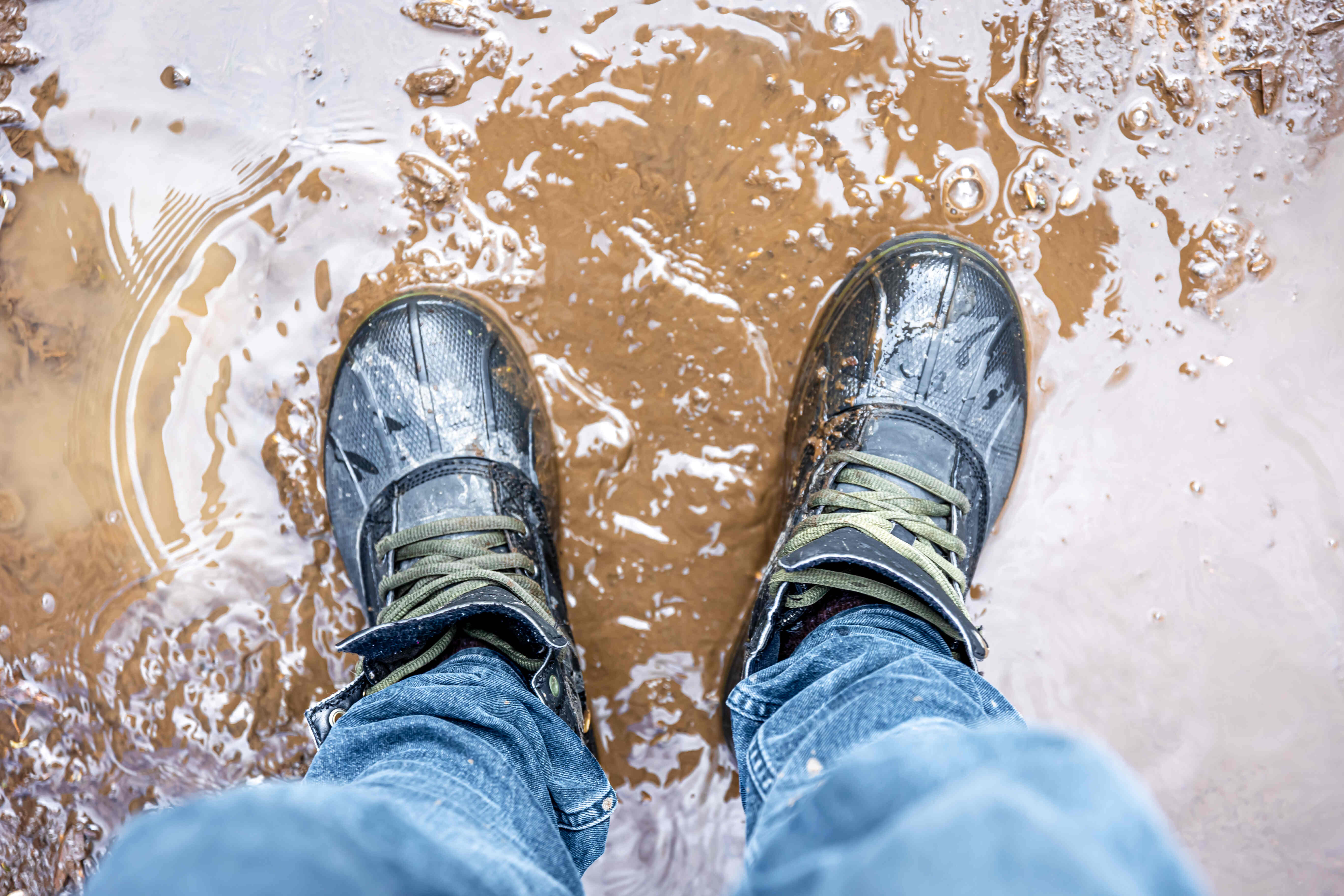 Blick auf nasse Schuhe, die in einer schlammigen Pfütze stehen.